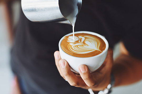 Man creating an artistic flower design by pouring cream in a cappuccino.