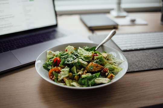 A fresh salad bowl on a desk next to a laptop.