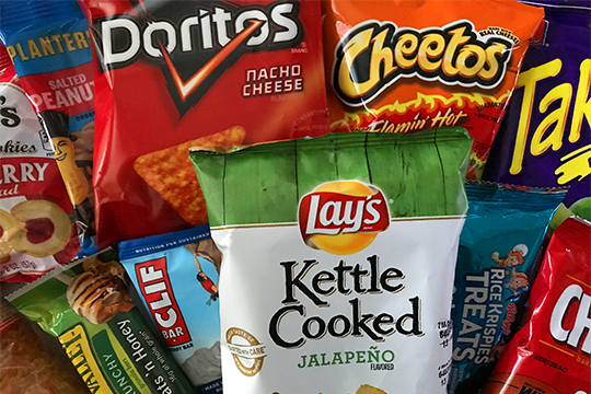 An assortment of snacks including: Lay's, Doritos, Cheetos, Takis, Clif Bar, and Planter's Peanuts.